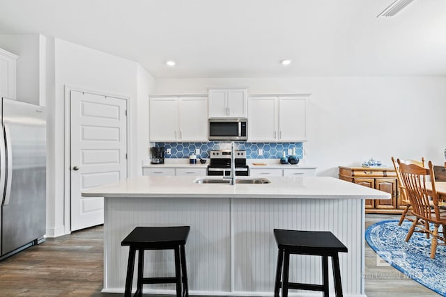 kitchen with tasteful backsplash, white cabinetry, sink, stainless steel appliances, and a center island with sink