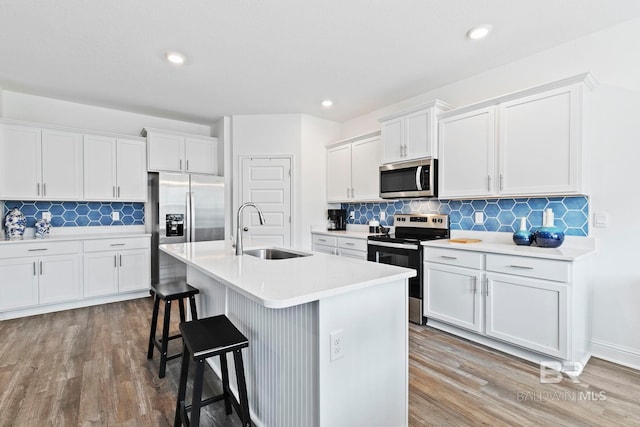 kitchen with stainless steel appliances, white cabinetry, sink, and an island with sink