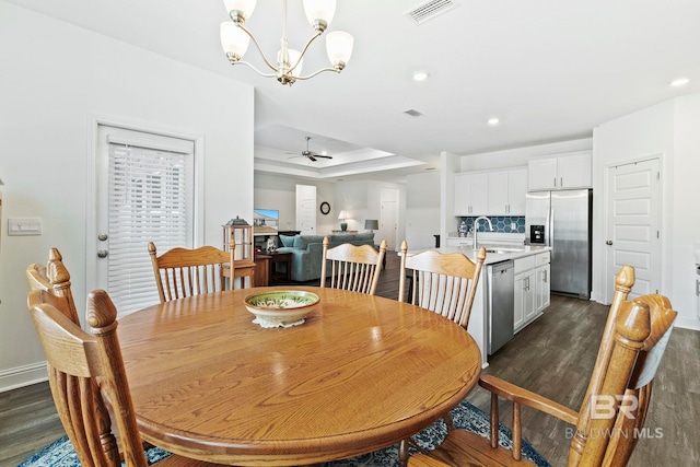 dining area featuring ceiling fan with notable chandelier, dark wood-type flooring, sink, and a tray ceiling