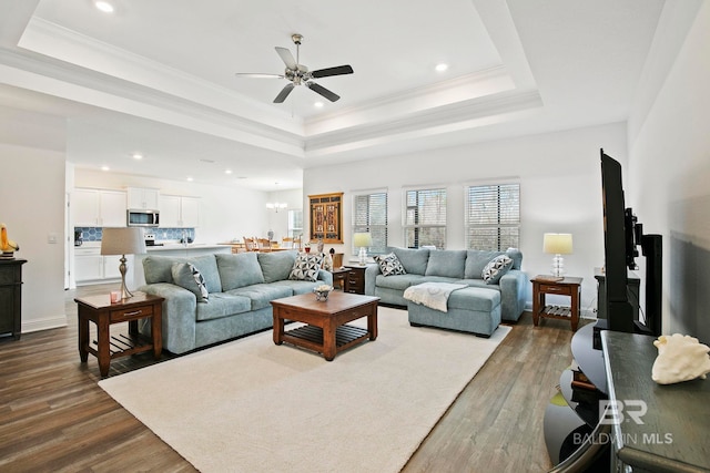 living room featuring a raised ceiling, ornamental molding, ceiling fan with notable chandelier, and dark hardwood / wood-style flooring