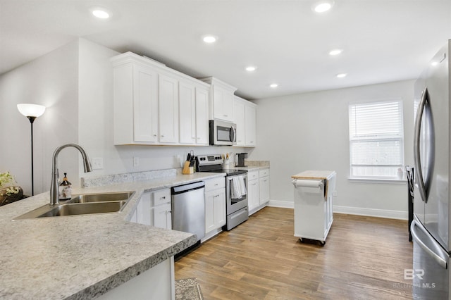 kitchen with light countertops, stainless steel appliances, light wood-type flooring, a sink, and recessed lighting