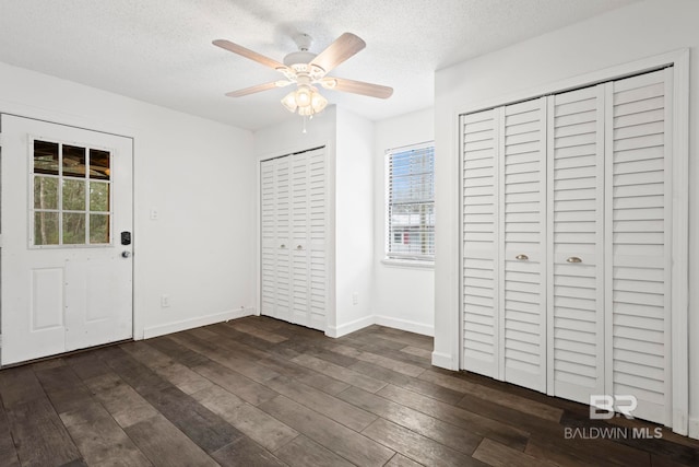 unfurnished bedroom featuring ceiling fan, a textured ceiling, dark hardwood / wood-style floors, and multiple closets