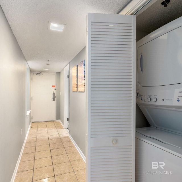 laundry room with light tile patterned floors, baseboards, stacked washing maching and dryer, laundry area, and a textured ceiling