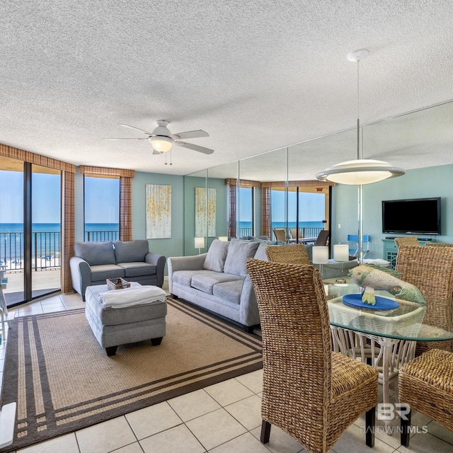 living area with light tile patterned floors, a water view, a textured ceiling, and a ceiling fan