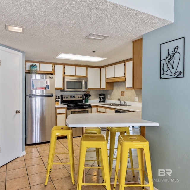 kitchen featuring light countertops, light tile patterned floors, appliances with stainless steel finishes, a peninsula, and a sink