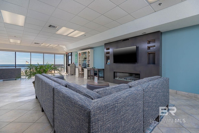 living room with a drop ceiling, visible vents, baseboards, and a glass covered fireplace