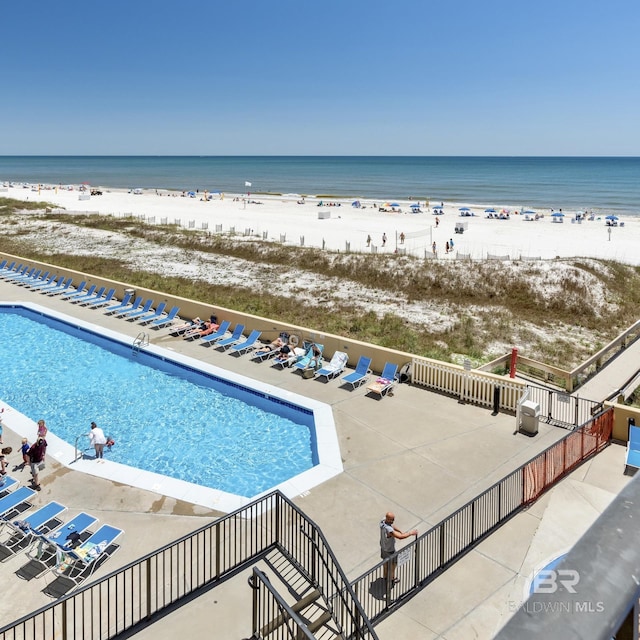 community pool with a patio, a water view, and a view of the beach