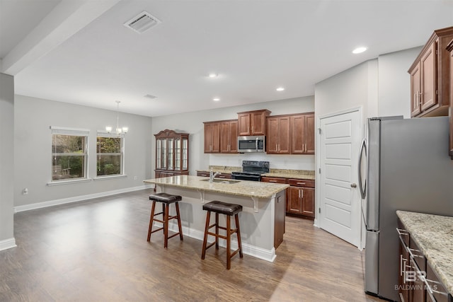 kitchen with a kitchen breakfast bar, stainless steel appliances, a center island with sink, a notable chandelier, and dark hardwood / wood-style floors