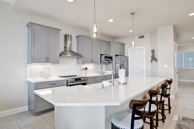 kitchen featuring wall chimney range hood, a breakfast bar area, appliances with stainless steel finishes, hanging light fixtures, and a center island with sink