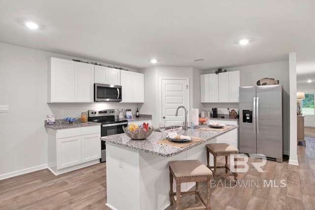 kitchen with a center island with sink, stainless steel appliances, white cabinetry, sink, and light hardwood / wood-style floors