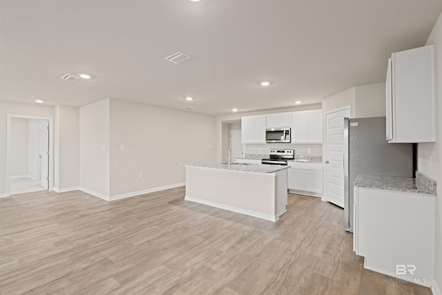 kitchen featuring appliances with stainless steel finishes, light stone counters, an island with sink, light hardwood / wood-style floors, and white cabinets