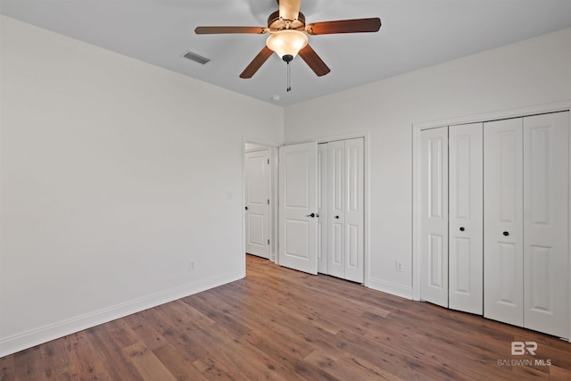 unfurnished bedroom featuring visible vents, baseboards, multiple closets, wood finished floors, and a ceiling fan