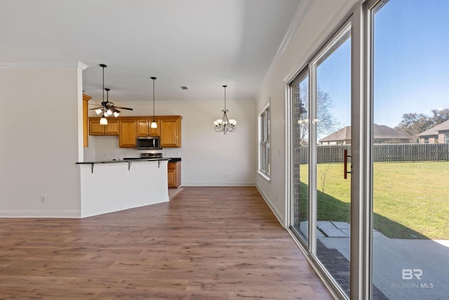 kitchen with wood finished floors, ornamental molding, dark countertops, stainless steel microwave, and decorative light fixtures