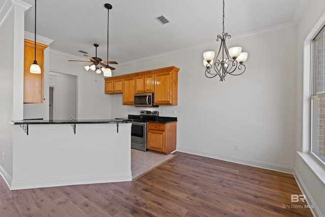 kitchen with dark countertops, ornamental molding, brown cabinets, appliances with stainless steel finishes, and wood finished floors