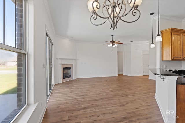 unfurnished living room with light wood finished floors, a sink, a tiled fireplace, crown molding, and ceiling fan with notable chandelier