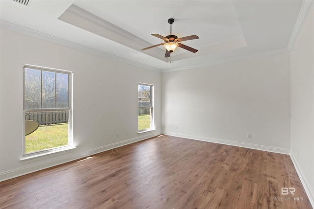 empty room featuring a tray ceiling, baseboards, wood finished floors, and ornamental molding