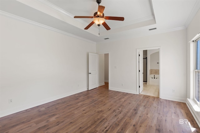 unfurnished bedroom featuring a tray ceiling, baseboards, wood finished floors, and ornamental molding