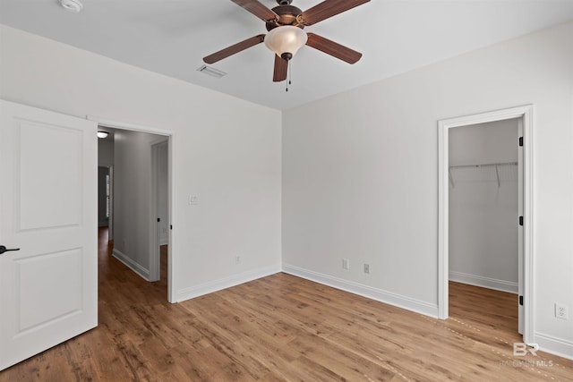 unfurnished bedroom featuring a spacious closet, visible vents, light wood-type flooring, and baseboards