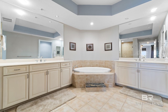 bathroom featuring a raised ceiling, vanity, tile patterned flooring, and tiled bath