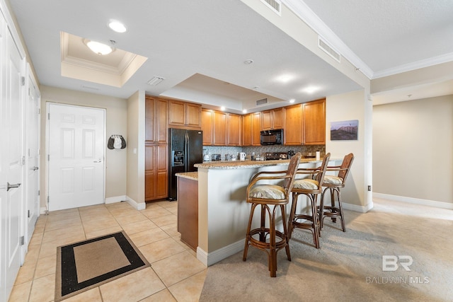 kitchen featuring tasteful backsplash, black appliances, a kitchen breakfast bar, light tile patterned floors, and a tray ceiling