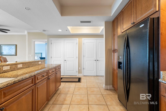 kitchen with light tile patterned flooring, black fridge, ornamental molding, a tray ceiling, and light stone countertops