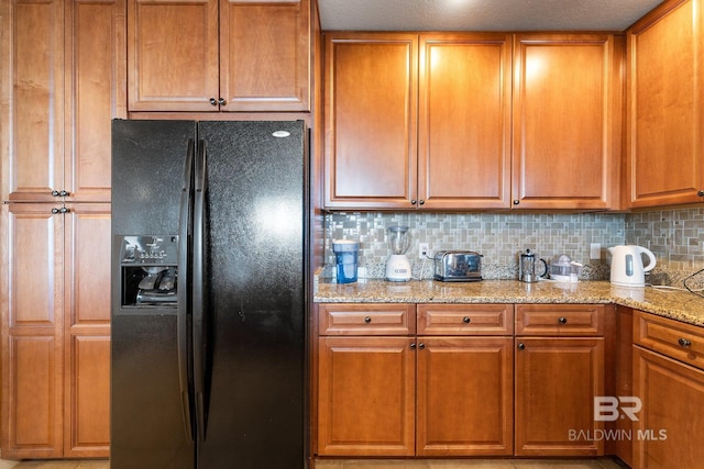 kitchen featuring light stone counters, backsplash, and black refrigerator with ice dispenser