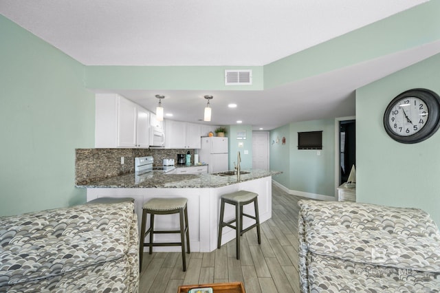 kitchen featuring kitchen peninsula, a breakfast bar, white cabinetry, light wood-type flooring, and white appliances