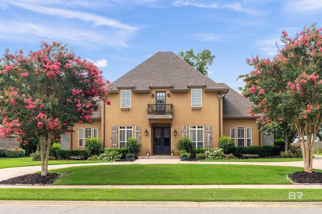 view of front of house featuring a front lawn, a balcony, and french doors