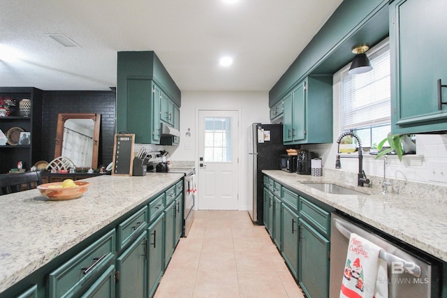 kitchen with appliances with stainless steel finishes, light stone counters, sink, green cabinets, and light tile patterned flooring