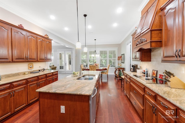 kitchen with dark hardwood / wood-style flooring, pendant lighting, an island with sink, crown molding, and light stone counters