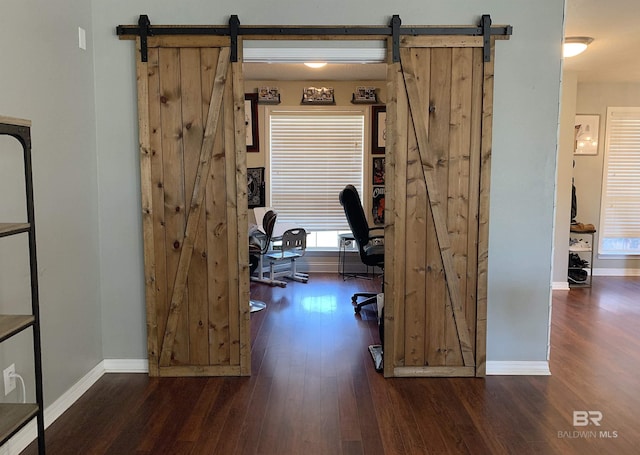 office space with baseboards, a barn door, and wood finished floors