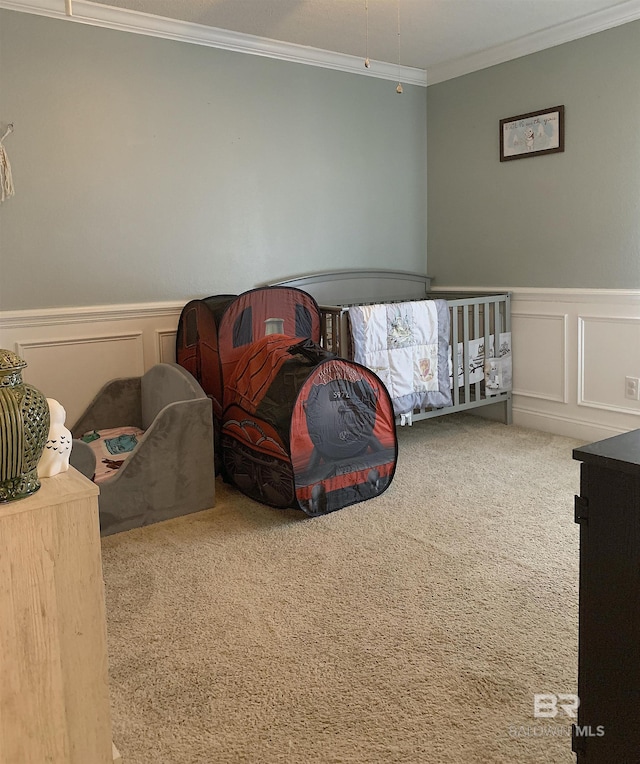carpeted bedroom with crown molding, wainscoting, and a decorative wall