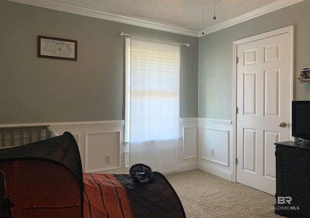 carpeted bedroom featuring crown molding, a textured ceiling, wainscoting, and a decorative wall