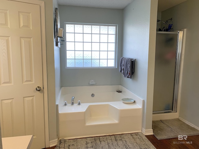 bathroom with wood finished floors, baseboards, a bath, and a shower stall