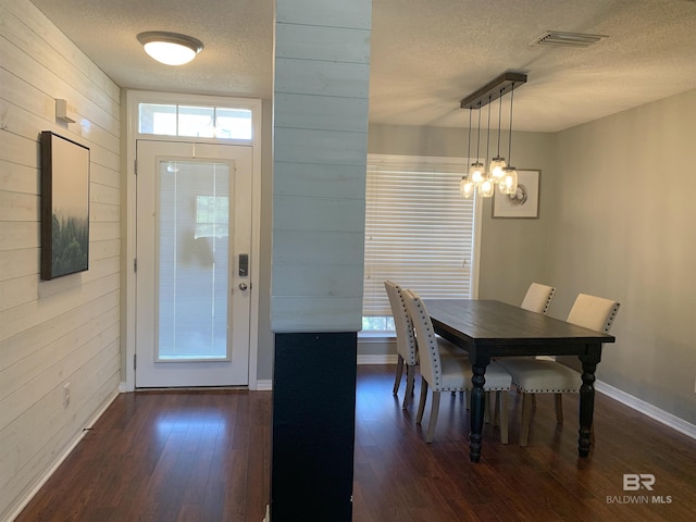 dining room with baseboards, wooden walls, dark wood-type flooring, a textured ceiling, and a chandelier