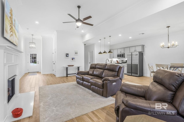 living room featuring crown molding, light hardwood / wood-style flooring, and ceiling fan with notable chandelier