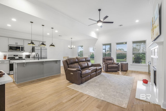 living room featuring sink, light hardwood / wood-style floors, ceiling fan with notable chandelier, and ornamental molding