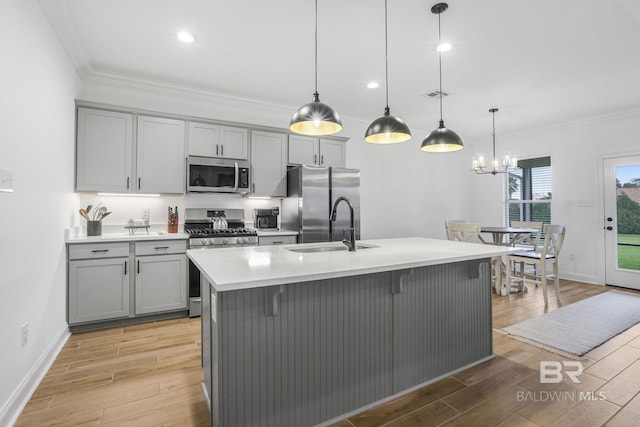 kitchen with stainless steel appliances, sink, decorative light fixtures, gray cabinets, and an island with sink