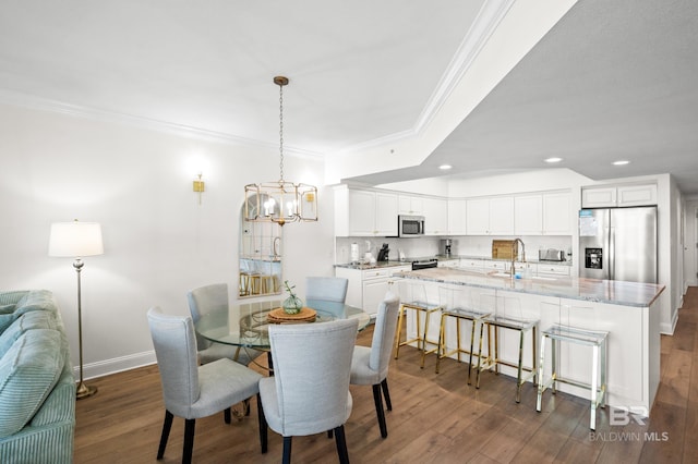 dining room with sink, dark hardwood / wood-style flooring, ornamental molding, and an inviting chandelier