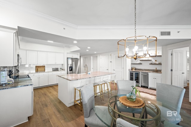 dining area with wood-type flooring, wine cooler, sink, a notable chandelier, and ornamental molding