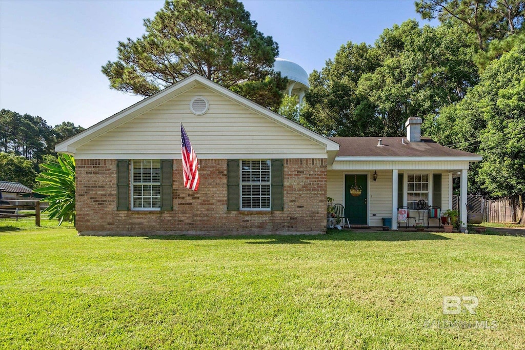 ranch-style house featuring brick siding, a chimney, covered porch, and a front yard