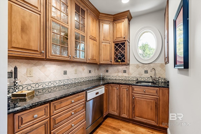 kitchen featuring brown cabinetry, dishwasher, dark stone counters, and a sink