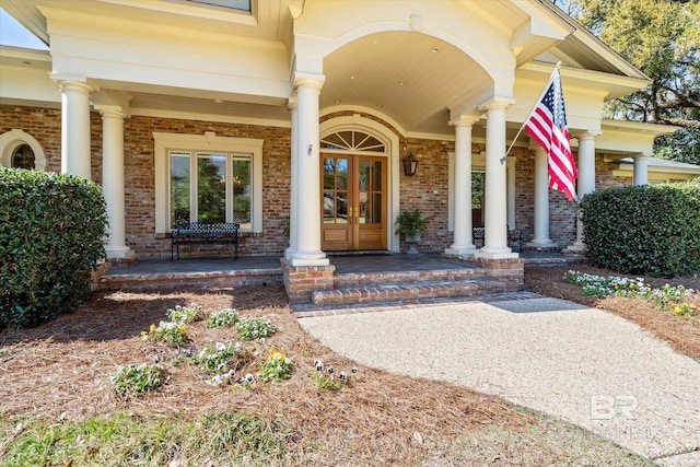 property entrance with a porch, french doors, and brick siding