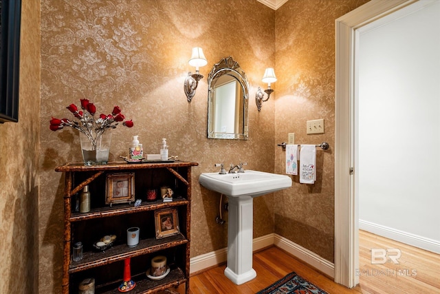 bathroom with a sink, wallpapered walls, baseboards, and wood finished floors