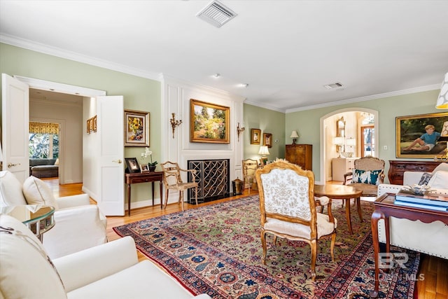 living area featuring visible vents, arched walkways, light wood-style flooring, and crown molding