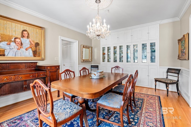 dining space with light wood-type flooring, ornamental molding, wainscoting, and a chandelier