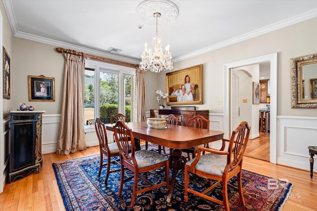 dining room featuring crown molding, wainscoting, light wood-type flooring, and a chandelier