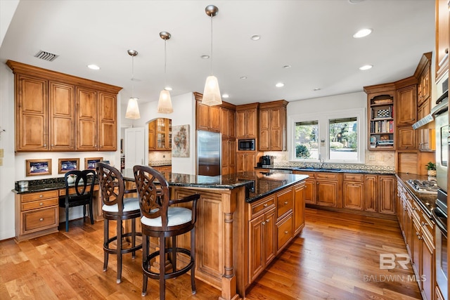 kitchen with light wood finished floors, built in appliances, brown cabinets, and a kitchen island