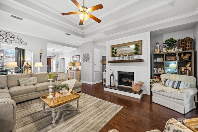 living room featuring a fireplace, a raised ceiling, crown molding, and dark wood-type flooring