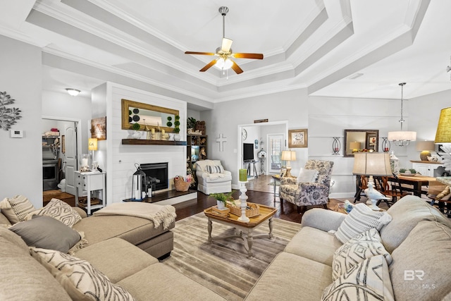 living room featuring a raised ceiling, crown molding, ceiling fan, a large fireplace, and wood-type flooring